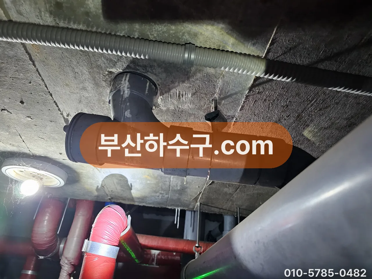 지하 천장 입상관 분기 T관 소제구로 스프링을 밀어 넣어 공용관 막힘 구간을 확인하는 장면