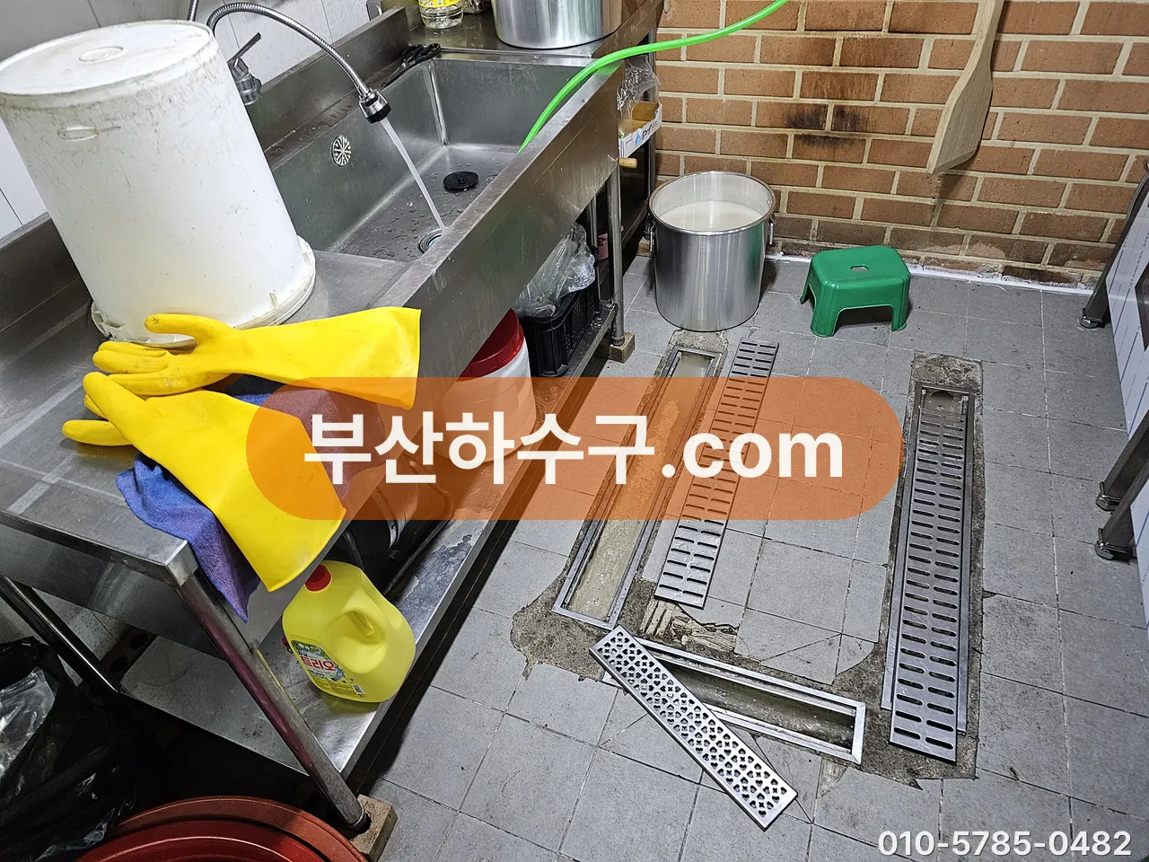 주방 싱크 옆 트렌치 그레이팅을 분리해 세척 전 배수로 안을 확인하는 모습