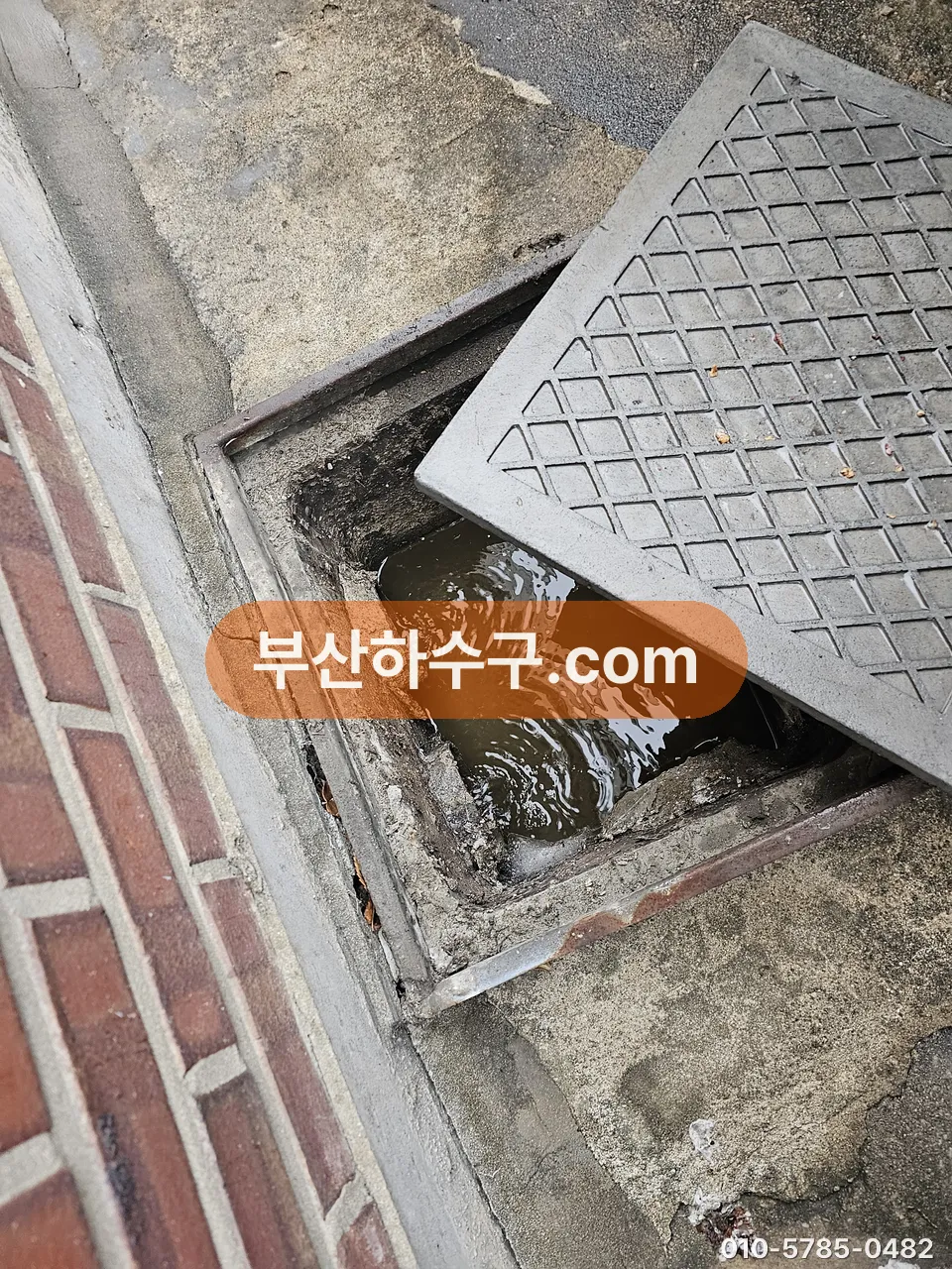 건물 옆 빗물받이 그레이팅을 들어내고 안에 고인 물과 토사를 확인하는 장면