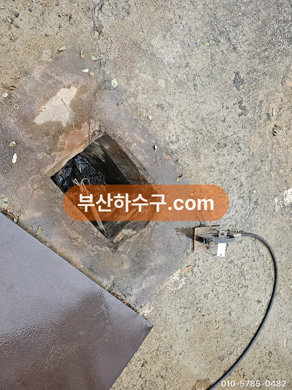 콘크리트 바닥 점검구를 열고 옥외 하수관에 케이블을 넣어 막힌 방향을 확인하는 모습