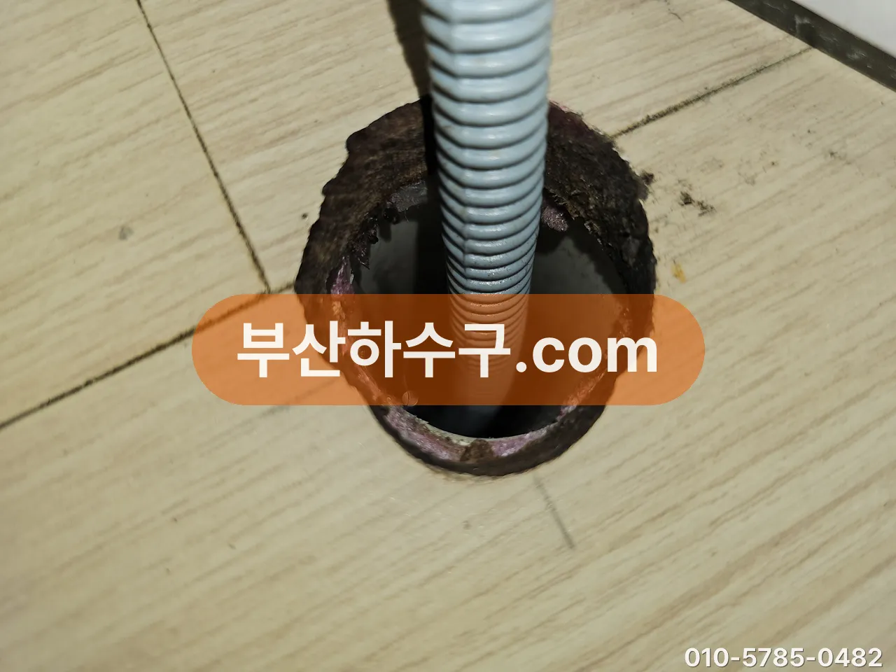바닥 배수구 트랩을 떼고 스프링 케이블을 관 안으로 넣어 보풀 뭉침을 끌어내는 장면